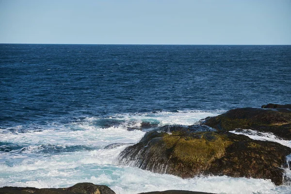 Μικρά κύματα της θάλασσας σπάνε στις πέτρες της ακτής. Μια φωτεινή ηλιόλουστη μέρα και λευκό αφρό των κυμάτων. Οι παγετώνες τήξης ως περιβαλλοντικές επιπτώσεις της ατμοσφαιρικής ρύπανσης. — Φωτογραφία Αρχείου
