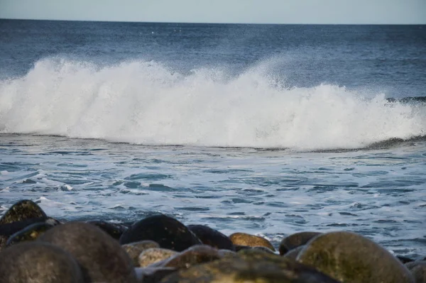 Pequeñas olas marinas rompen contra las piedras de la orilla. Un día soleado brillante y espuma blanca de las olas. El derretimiento de los glaciares como impacto ambiental de la contaminación atmosférica. —  Fotos de Stock