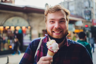 Yüz maskesi takan bir adam, koronavirüsten korunuyor. Covid-19 kişisi. Corona virüsünün ortasında oturmuş dondurmasını yemeye çalışıyor..