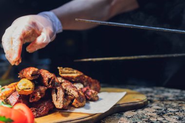 Siyah eldivenli adam beyaz tabakta yemek için spatulayla kuzu eti koydu. Lezzetli pişmiş kuzu eti.