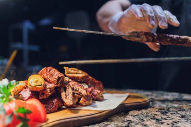 Siyah eldivenli adam beyaz tabakta yemek için spatulayla kuzu eti koydu. Lezzetli pişmiş kuzu eti.