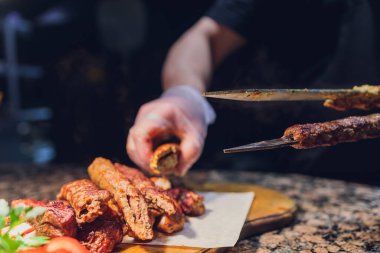 Siyah eldivenli adam beyaz tabakta yemek için spatulayla kuzu eti koydu. Lezzetli pişmiş kuzu eti.