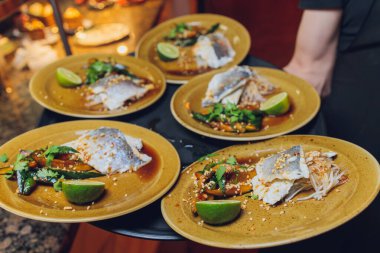 Lüks bir restoranda garsonların servis ettiği enginar ve sulu soslu domuz filetosu..