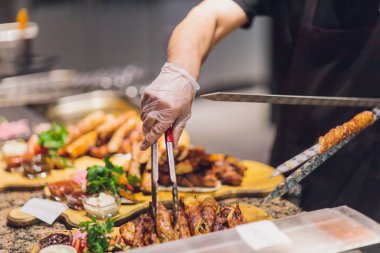 Siyah eldivenli adam beyaz tabakta yemek için spatulayla kuzu eti koydu. Lezzetli pişmiş kuzu eti.