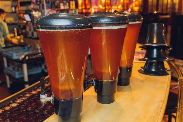 Sluiten op een grote pint gevuld met ongefilterde tarwe ale, voor 3 bier en cider glazen, met vrouw op de achtergrond, op een houten tafel in een ambachtelijke brouwerij. — Stockfoto