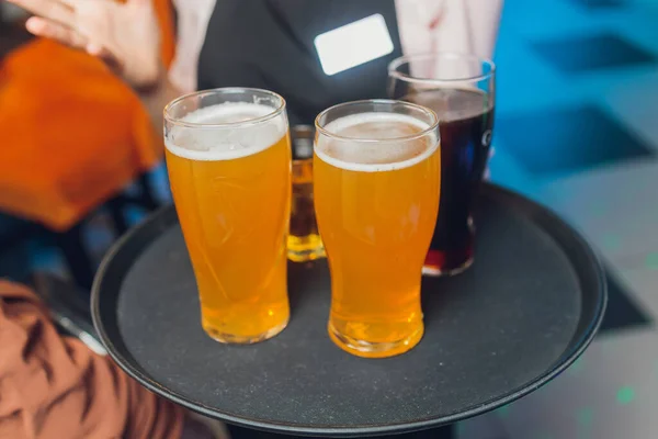 Κοντινό πλάνο σε μια μεγάλη μπύρα γεμάτη με αφιλτράριστο σιτάρι ale, μπροστά από 3 μπύρες και ποτήρια μηλίτη, με γυναίκα στο παρασκήνιο, σε ένα ξύλινο τραπέζι σε ένα ζυθοποιείο βιοτεχνίας. — Φωτογραφία Αρχείου