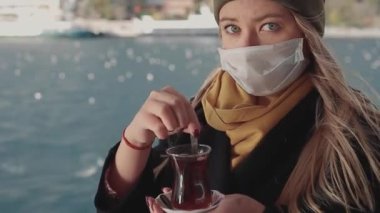 Bir kadın eli, dalgalı su ve uzaktan İstanbul 'daki sisli Bakireler Kulesi' nin arka planında Türk salep sahlep adlı tarçınlı sıcak sütlü bir bardak tutuyor..