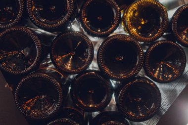 Yakın çekim, mahzende eski şarap şişeleri. Uzun depolama nedeniyle tozla kaplı cam şarap dolapları. Sıcak, sessiz tonlar. Şişe metni.