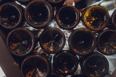 Yakın çekim, mahzende eski şarap şişeleri. Uzun depolama nedeniyle tozla kaplı cam şarap dolapları. Sıcak, sessiz tonlar. Şişe metni.