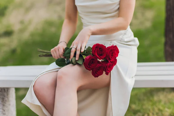 Primer plano de la mano de mujer joven sosteniendo flores de rosa roja en el fondo al aire libre. — Foto de Stock