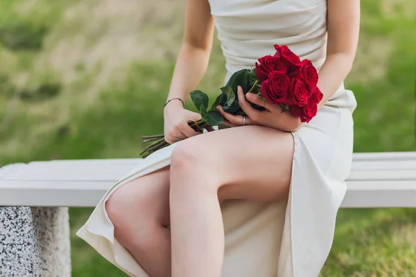 Nahaufnahme einer jungen Frau, die rote Rosenblumen auf dem Hintergrund hält. — Stockfoto