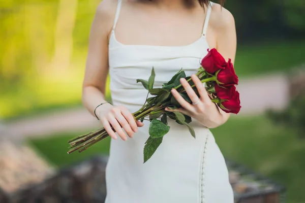 Close up de jovem mão segurando flores vermelhas rosa no fundo ao ar livre. — Fotografia de Stock