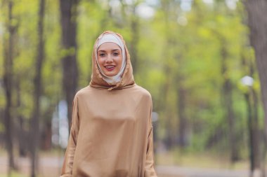 Müslüman elbiseli güzel bir kadın yaz parkı arka planında duruyor sonbahar ağaçları. Dünya tesettür günü..