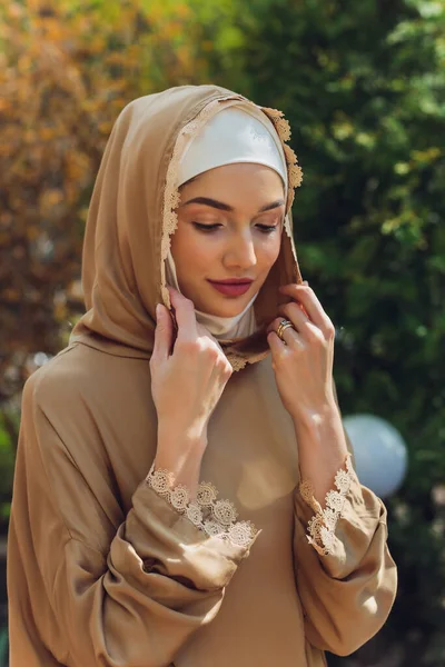 Islamitische prachtige vrouw in een islamitische jurk staande op een zomer park straat achtergrond bos herfst bomen.wereld hijab dag. — Stockfoto