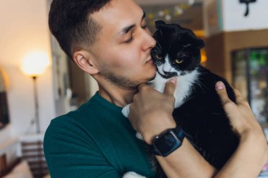 Tişörtlü genç adam elinde kedi tutuyor..