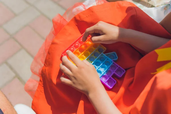 Ανώνυμο παιδί κρατά στα χέρια του αισθητηριακό παιχνίδι pop αυτό και το δείχνει μπροστά από τον εαυτό του.Χρώμα Rainbow.. — Φωτογραφία Αρχείου