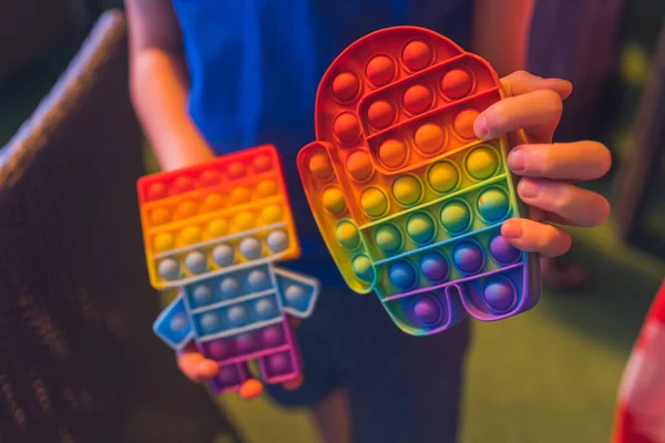 Criança anônima segurar em suas mãos brinquedo sensorial pop-lo e mostra-o na frente de si mesmo. Rainbow color.Antistress brinquedo para crianças e adultos. — Fotografia de Stock