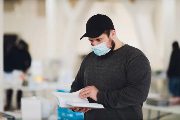 コロナウイルスの流行の間に図書館で読書の本を勉強している人は、保護医療面マスクを着用して、 19パンデミックをカバーします。図書館員のための新しい標準. — ストック写真