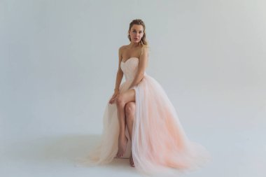 Pembe elbiseli orta yaşlı sarışın kadın gri arka planda poz veriyor..