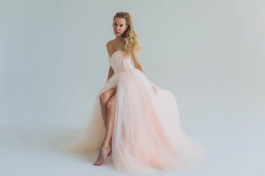 Pembe elbiseli orta yaşlı sarışın kadın gri arka planda poz veriyor..