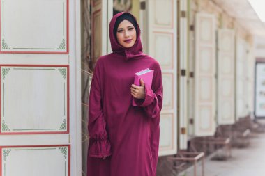 Kendine güvenen Arap işadamı Dubai 'de yürüyor ve gülümsüyor. Arap İşletmeleri başörtüsü Dubai 'nin gökdelenlerine karşı sokaklarda. Kadın siyah bir abaya giymiş..