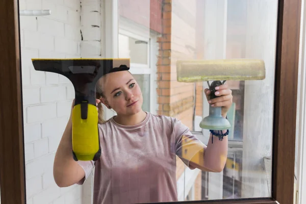 Красива молода домогосподарка в робочому одязі миє вікна професійними інструментами вдома . — стокове фото