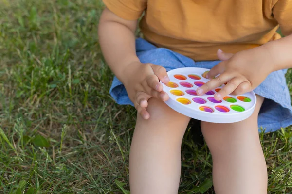 Colorido antistress brinquedo sensorial violeta empurrá-lo pop-lo em mãos de crianças. Antistress moda pop-lo brinquedo. Arco-íris fidget sensorial. Novo brinquedo de silicone na moda. — Fotografia de Stock