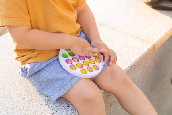 Colorido antistress brinquedo sensorial violeta empurrá-lo pop-lo em mãos de crianças. Antistress moda pop-lo brinquedo. Arco-íris fidget sensorial. Novo brinquedo de silicone na moda. — Fotografia de Stock