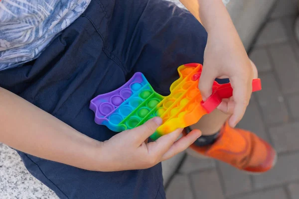 Juguete sensorial colorido antiestrés nervioso empuje pop en las manos de los niños pequeños. Antiestrés de moda pop it toy. Arco iris nerviosa sensorial. Nuevo juguete de silicona de moda. — Foto de Stock