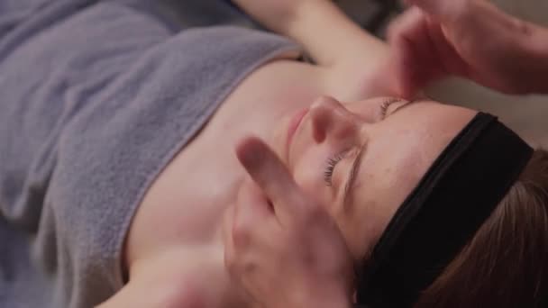 Sluiten van masseuse handen masseren vrouwelijk gezicht. Vrouw gesloten ogen met plezier. — Stockvideo