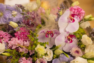 Tuğla duvara karşı farklı taze çiçeklerden oluşan renkli bir buket. Bir demet orkide, güller, frezya ve okaliptüs yaprakları. Kırsal çiçek arka planı. Üst görünüm.