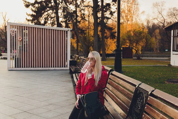 Hermosa mujer de moda con bolso sentado y esperando en un banco en el parque y beber agua. — Foto de Stock