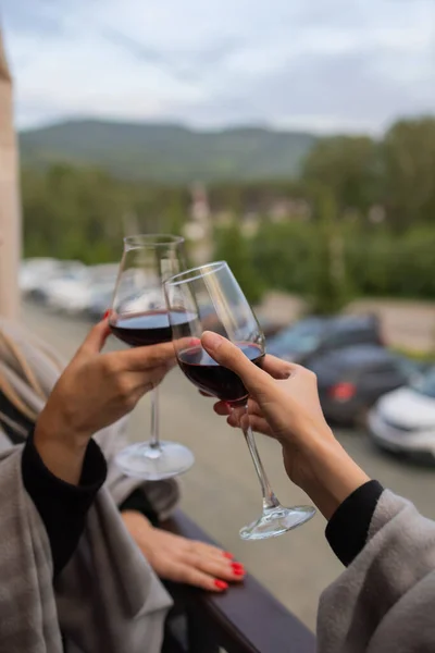 Two people clinking with glasses of red wine, celebrating success or speaking toast in wine restaurant, against racks with wine bottles, close up.