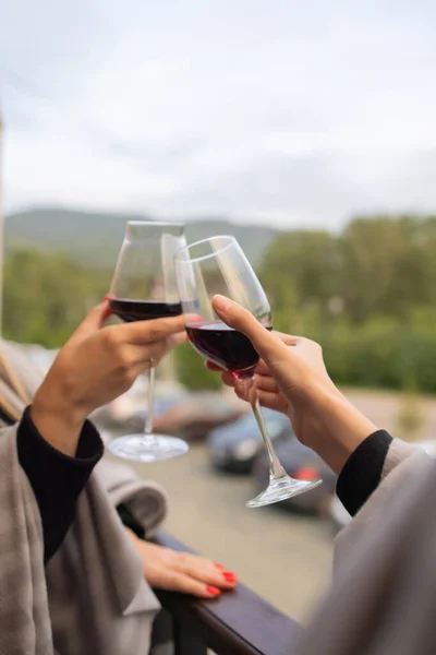 Two people clinking with glasses of red wine, celebrating success or speaking toast in wine restaurant, against racks with wine bottles, close up.