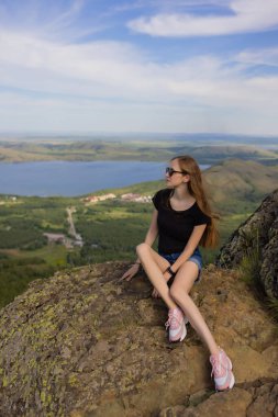 Sırt çantalı kadın yürüyüşçü dağın tepesinde oturuyor ve gün boyunca manzaranın tadını çıkarıyor..
