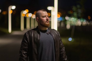 Bir adam sokak kenti boyunca yürür. Arka planda fenerlerle süslenmiş bir caddede genç bir adamın portresi var..