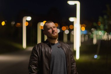 Bir adam sokak kenti boyunca yürür. Arka planda fenerlerle süslenmiş bir caddede genç bir adamın portresi var..