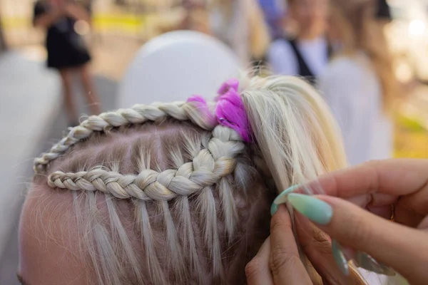 As mãos de mulheres tecem um pigtail na cabeça de morenas. — Fotografia de Stock