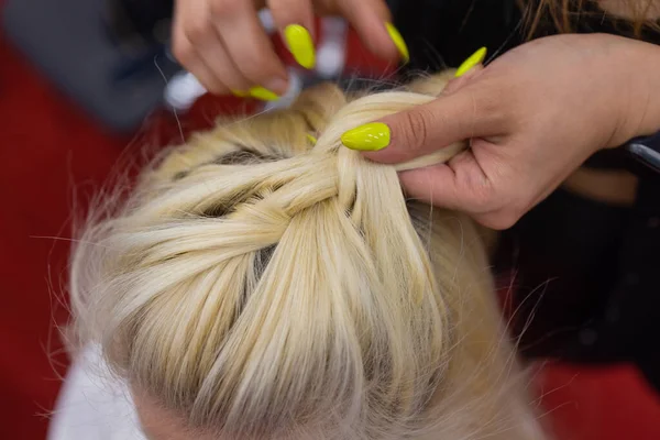 As mãos de mulheres tecem um pigtail na cabeça de morenas. — Fotografia de Stock