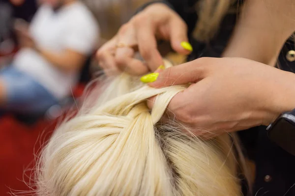 Les mains des femmes tissent une queue de cochon sur la tête des brunes. — Photo