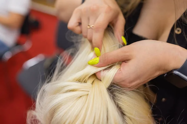 As mãos de mulheres tecem um pigtail na cabeça de morenas. — Fotografia de Stock