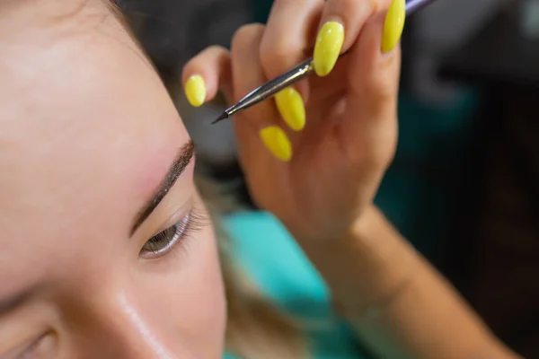 Kosmetikerin macht Enthaarung mit Wachsstreifen junge Frauen Augenbrauen im Wellnesszentrum. Attraktive Frau bekommt Gesichtsbehandlung im Schönheitssalon. — Stockfoto