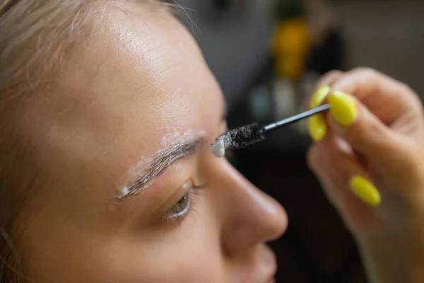 Kosmetyk robiący depilację woskowym paskiem młodych kobiecych brwi w centrum spa. Atrakcyjna kobieta otrzymuje pielęgnację twarzy w salonie piękności. — Zdjęcie stockowe
