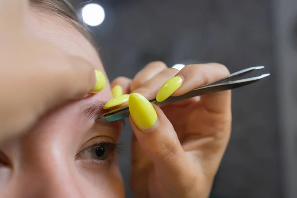 Kosmetolog gør depilation med voksstrimmel unge kvinders øjenbryn i spa center. Attraktiv kvinde får ansigtspleje på skønhedssalon. - Stock-foto