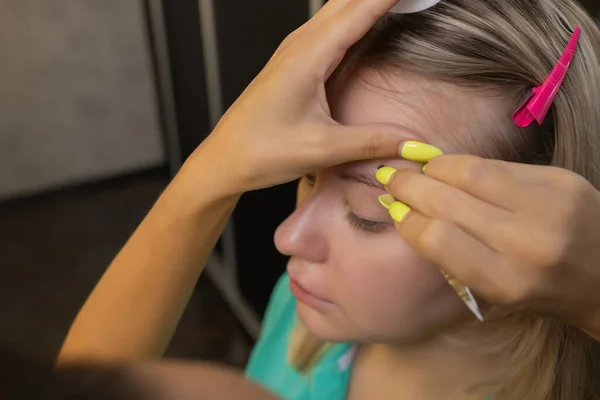 Kosmetyk robiący depilację woskowym paskiem młodych kobiecych brwi w centrum spa. Atrakcyjna kobieta otrzymuje pielęgnację twarzy w salonie piękności. — Zdjęcie stockowe