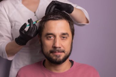Saç için mezoterapi. Çekici bir adam kafasından iğne vuruluyor. Güzellik salonunda mezoterapi gören bir adam, şırıngalı koruyucu eldivenli bir terapist.,