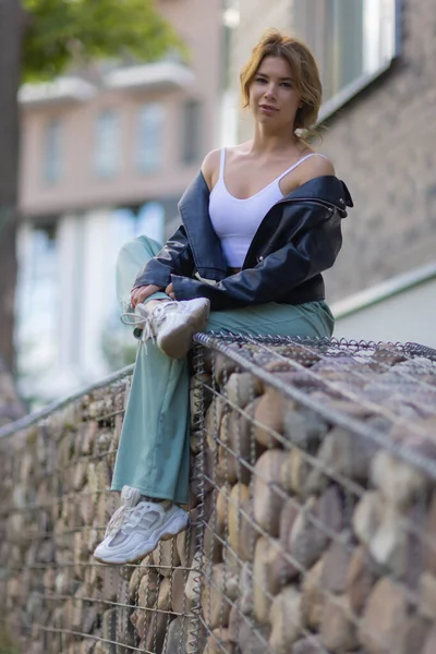 Portret van een jonge mooie vrouw in blauwe shorts zittend op een bankje op de binnenplaats van een wooncomplex. — Stockfoto