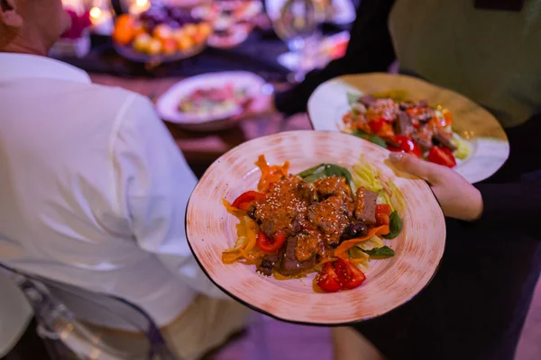 Dos platos de carne con hojas de ensalada y ensalada de verano en mano de camareros. — Foto de Stock