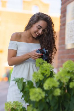 Yaz şehrinde yürürken aynasız kamera kullanan genç ve çekici bir kız öğrenci ya da turist. Kadın fotoğraf çeker ve havanın tadını çıkarır..