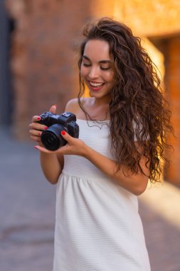 Yaz şehrinde yürürken aynasız kamera kullanan genç ve çekici bir kız öğrenci ya da turist. Kadın fotoğraf çeker ve havanın tadını çıkarır..